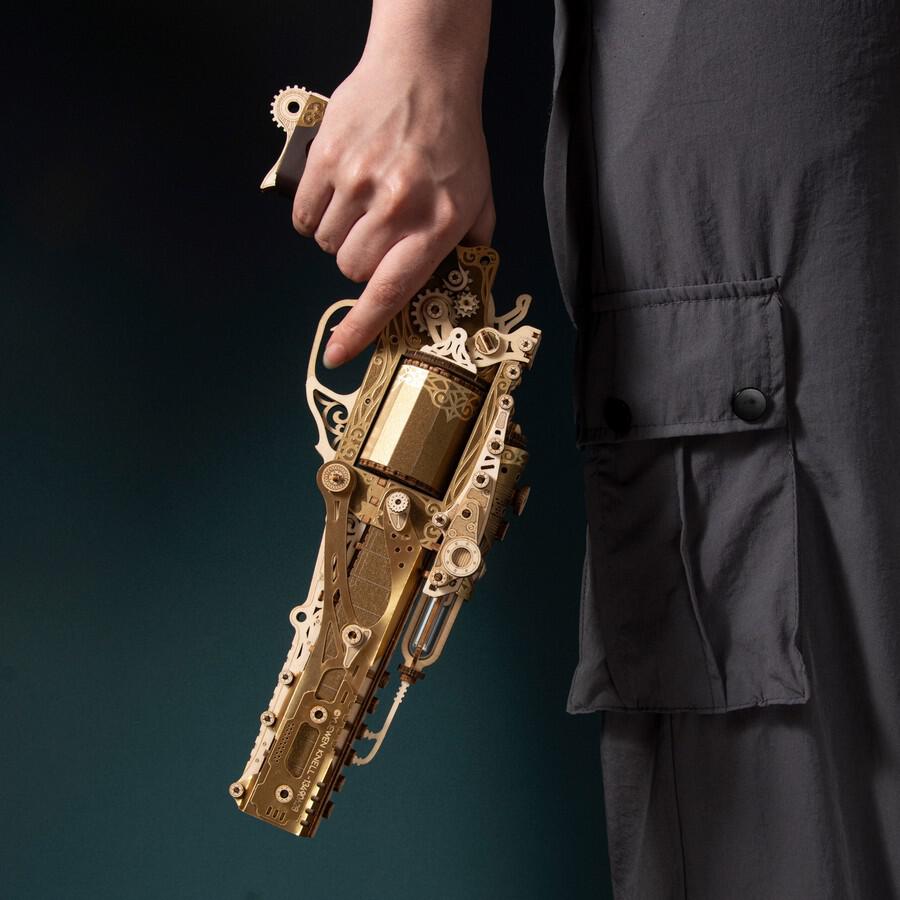 HowCat Steampunk Revolver Gold DIY 3D Wooden & Paper Puzzle held in hand against a dark background.